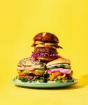 Three burgers in a stack on a teal plate, with a yellow background
