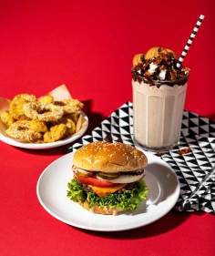 Burger on a white plate with chocolate cookie shake, and fried pickles on a red background