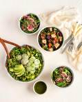 Several bowls of different types of salad on a light stucco background with cheesecloth on the side